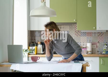 Focused female designer or architect work from home check building blueprint with online documents Stock Photo