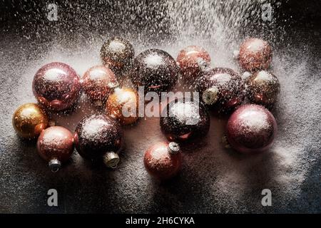 Top view of various shiny Christmas balls on black table being poured with white decorative snow Stock Photo