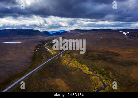 Aerial view of a winding asphalt road cutting through lush green ...