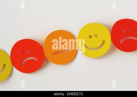 Chain of yellow, orange and red paper faces with positive, neutral and negative expression on white background Stock Photo