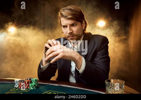 A man in a business suit sitting at the game table. Male player. Passion, cards, chips, alcohol, dice, gambling, casino - it is as male entertainment. Stock Photo