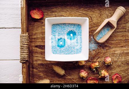 Blue and white granulated wax crystals to create candles by pouring in bowl and inserting wick. Handmade sand candle in white ceramic bowl on wooden t Stock Photo