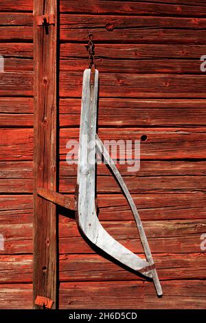 a very old agricultural tool made of wood hanging on a red barn Stock Photo