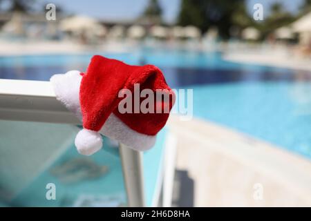 Santa claus hat put on lawn chair near swimming pool with clean turquoise water Stock Photo