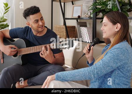 Happy man playing guitar and looking at pretty smiling singing girlfriend Stock Photo