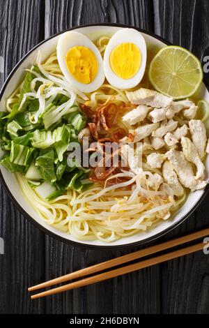 Soto ayam Indonesian chicken noodle soup close up in the plate on the table. Vertical top view from above Stock Photo