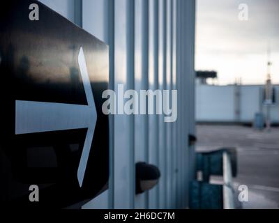 Directional exit right arrow sign in black and white on the metal wall at the rooftop parking of a shopping mall in the evening dusk. Stock Photo