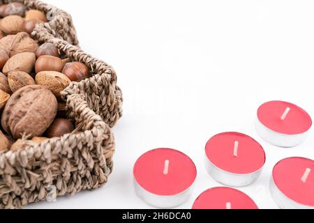 High angle detail studio shot of basket full of mixed nuts and red tea candles isolated on white background. Christmas concept. Stock Photo