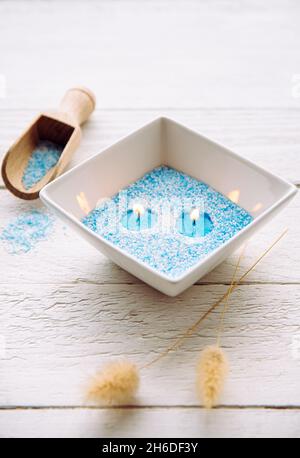 Blue and white granulated wax crystals to create candles by pouring in bowl and inserting wick. Handmade sand candle in white ceramic bowl on wooden b Stock Photo