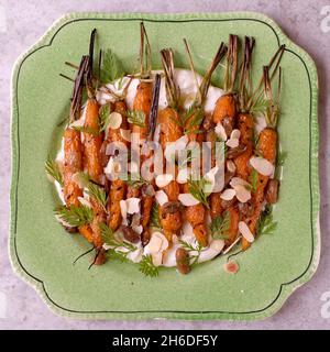 Cumin-roasted carrots on a bed of ricotta, garnished with flaked almonds and chopped carrot tops Stock Photo
