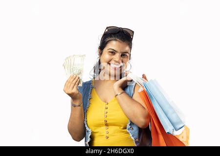 A beautiful Indian woman in yellow dress with shopping bags and Indian currencies smiling at the camera on white background Stock Photo