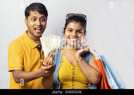 Indian couple in yellow dress with shopping bags and big savings smiling on white background Stock Photo