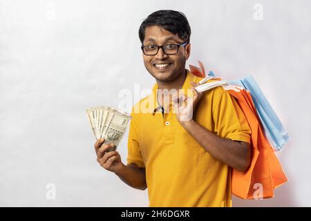A middle aged Indian man in yellow dress with shopping bags and cash smiling at the camera on white background Stock Photo