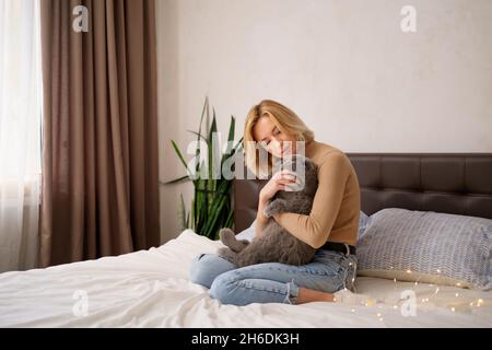 Pets, morning, comfort, rest and people concept - happy young woman with cat in bed at home Stock Photo