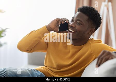 Joyful black man reclining on couch, having phone conversation Stock Photo