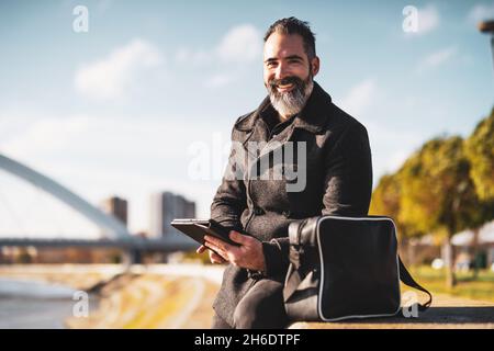 Businessman is sitting outdoor in the city and using digital tablet. Stock Photo