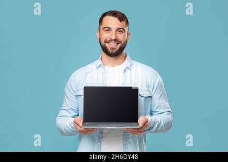 Friendly glad adult european man showing laptop with blank screen, isolated on blue background, free space Stock Photo