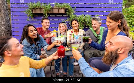 happy diverse group of friends celebrating new year eve making a celebratory toast clinking beautiful gourmet cocktail glasses in outdoor party bar re Stock Photo