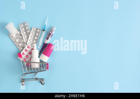 Various medicines, syringe, thermometer in shopping cart on blue background. Pharmacy sale concept. Copy space Stock Photo
