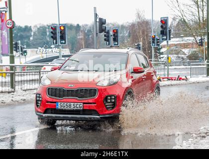 Car driving on town centre road, splashing through large puddle as melting snow creates flood water problems for traffic, Kidderminster, UK. Stock Photo