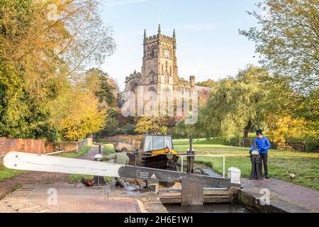 Narrowboat on the canal waterways approaching Kiddermister lock in summer with St Mary's church behind, Worcestershire, UK. Stock Photo
