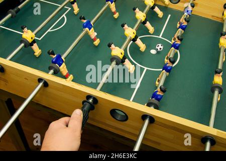 Hand holds the control stick of toy soccer players while playing table football Stock Photo