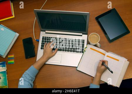 Top view of the home workplace. Female hands on laptop keyboard and open diary Stock Photo
