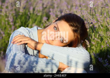 Beauty woman with blue eyes sitting in lavender field looking at you Stock Photo