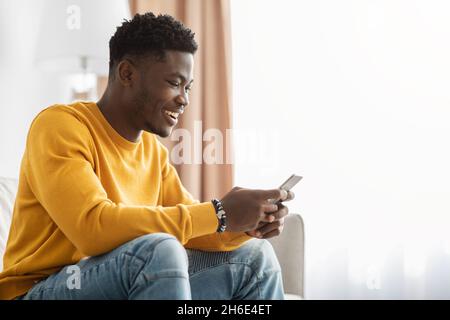 Happy black guy chatting with girlfriend, using smartphone at home Stock Photo