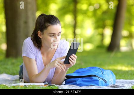 Serious student checking smart phone content lying in a campus Stock Photo