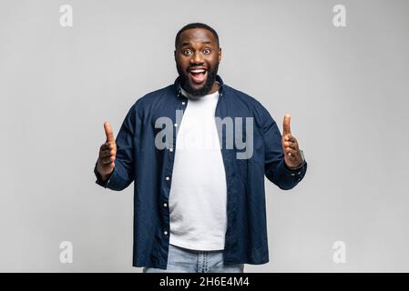 Advertising concept. Excited happy African-American guy demonstrating size of product with hands, measuring empty space, over grey background. Black man holds imagined object, something in palms Stock Photo