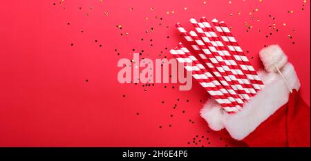 Red drinking cocktail party straws in Santa hat. New Year or Christmas flat lay top view Xmas holiday celebration decoration red paper background with Stock Photo