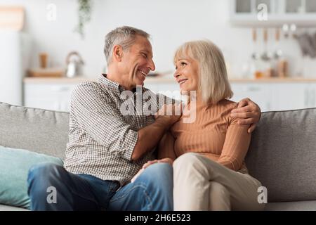 Cheerful Mature Husband Embracing Happy Wife Sitting At Home Stock Photo