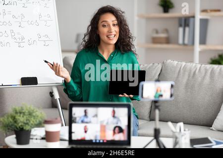 Female teacher explaining math online showing tablet to students Stock Photo
