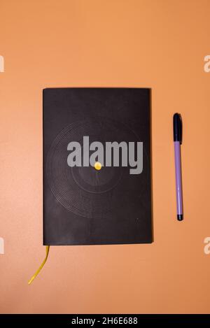 Black notebook with purple pen on orange background Stock Photo