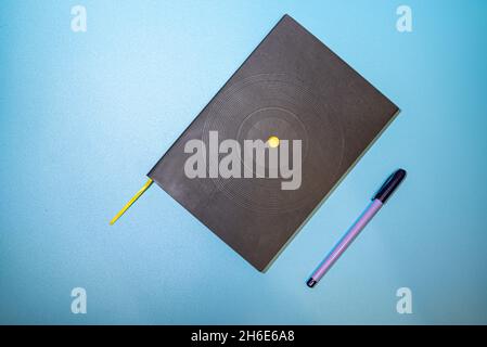 Black notebook with purple pen on blue background Stock Photo