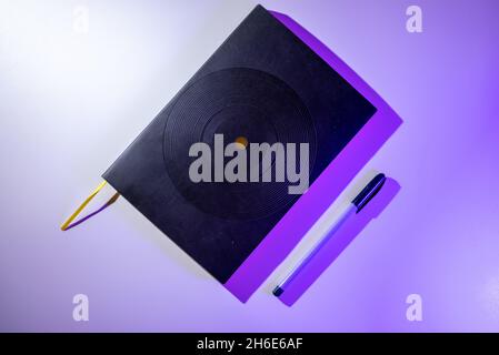 Black notebook with purple pen on purple background Stock Photo