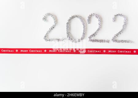 Happy new year 2022 written with foil and new year rain on an isolated white background along with a ribbon with the inscription merry christmas Stock Photo