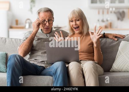 Emotional Mature Couple Using Laptop Computer Shouting In Excitement Indoor Stock Photo
