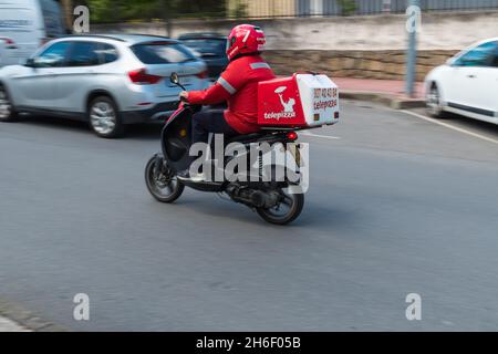 PLASENCIA, SPAIN - May 11, 2021: A pizza delivery man driving a Scooter-type motorcycle from the Telepizza chain delivers pizzas at home Stock Photo