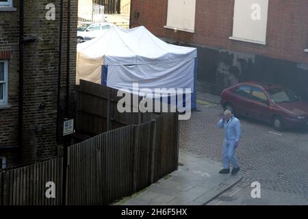 A police forensics officer attends the scene in Kilburn, north London, following the discovery of a body wrapped in sheets. Officers were called to the scene at 7.10am, after a member of the public made the discovery behind some shops. Stock Photo