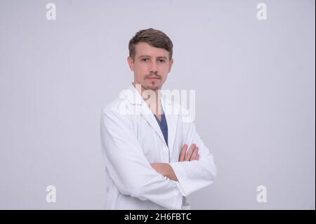 Portrait of young caucasian male medical doctor in white medical gown standing with crossed arms. Isolated on white. Looking at camera with copy space Stock Photo