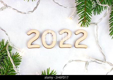Wooden numbers 2022 silhouette with Christmas lights and green fir tree branches on light background. New Year beginning congratulations and planning Stock Photo