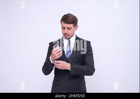 Portrait of elegant young caucasian handsome businessman in formal suit standing Isolated on white background in studio. Straightening cufflinks Stock Photo