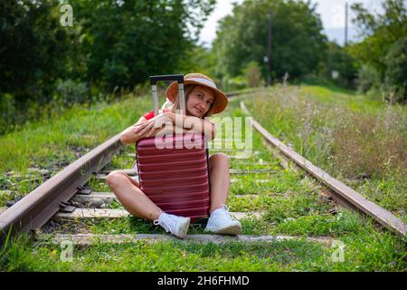 in sneakers the traveler sits on the rails with a suitcase Stock Photo