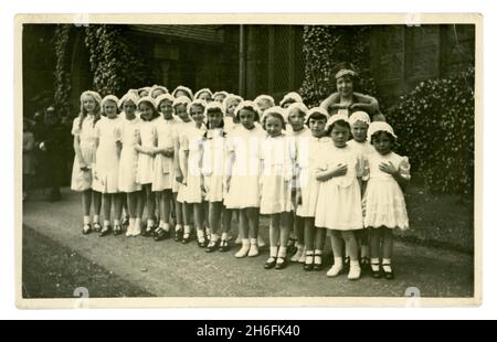 Original 1940's era postcard of young girl's Walking Day. The children are standing in the grounds of a church, they are possibly Sunday School attendees. The young girls are all dressed in white with lace caps, teacher in background in fur stole written on reverse is Miss E. Riley, 37 Rydal Road, church is Christ Church, Heaton, Rydal Road, Bolton, Lancashire, U.K. Stock Photo