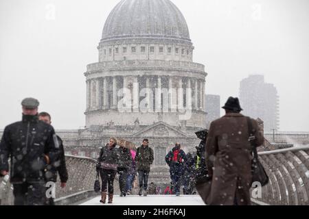 Commuters make their way across the millennium bridge in the snow in London this morning. Stock Photo
