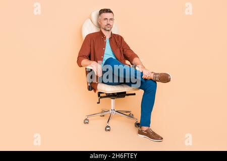 Full length photo of bossy smart partner middle-aged guy sit leather chair isolated over pastel beige color background Stock Photo