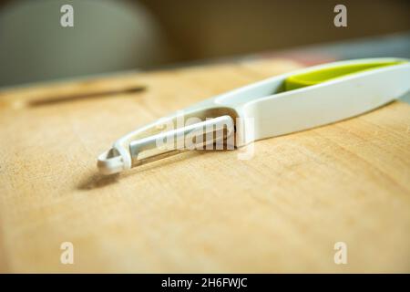 A kitchen tool for peeling vegetables is lying on a wooden board, closeup Stock Photo