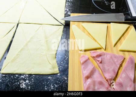 preparation of croissants, stuffed with ham and cheese and painted with egg yolk, on a wooden board, ready to bake Stock Photo